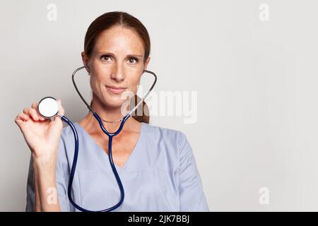 Kopfaufnahme der Frau professiona medizinische Arbeiter trägt blauen medizinischen Mantel mit Stethoskop, Porträt Stockfoto