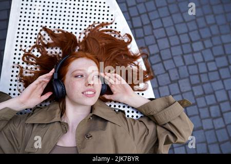 Teen Redhead Mädchen trägt Kopfhörer Musik im Freien hören Blick auf Kopieplatz. Stockfoto