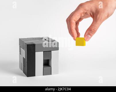 Hand setzen letzte herausragende Element in Puzzle-Würfel. Gelber Block in schwarz-weißer Bauweise. Erfolgreiches Abschlusskonzept. Hochwertige Fotos Stockfoto