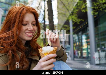 Lächelndes, cooles Teenager-Hipster-Mädchen, das Eis auf der städtischen Straße der Großstadt isst. Stockfoto