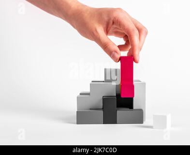 Frau Montage Tetris Puzzle. Hand Putting herausragende rote Element in schwarz-weiß-Konstruktion. Formationskonzept. Kreative einzigartige Idee. Logisches Spielzeug aus Holz. Hochwertige Fotos Stockfoto