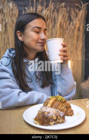 Eine junge Frau isst Croissants mit Kaffee in einem Café. Stockfoto