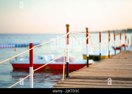 Stimmungsvoller hölzerner Steg über dem wunderschönen Strand mit blauem Himmel, hölzerner Steg mit kleinen Booten bei Sonnenuntergang im Sommer. Stockfoto