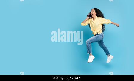 Frau, Die Am Telefon Spricht, Läuft In Der Luft, Blauer Hintergrund Stockfoto