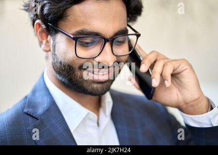 Lächelnder indischer Geschäftsmann in Anzug, der im Büro telefoniert. Stockfoto