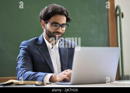 Junger indischer Geschäftsmann im Anzug, der an einem Laptop im Büro sitzt. Stockfoto