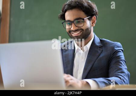 Lächelnder indischer junger Geschäftsmann, der Anzug trägt, der auf einem Laptop arbeitet. Stockfoto