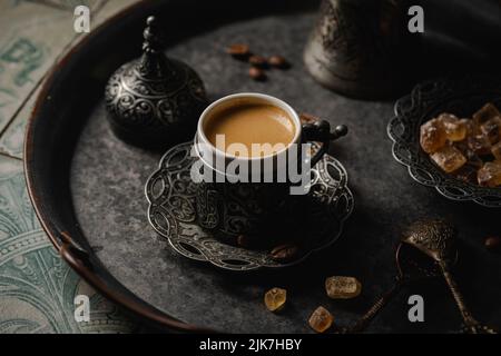 Kaffee in türkischer Metalltasse und Kaffeebohnen auf gefliestem Hintergrund Stockfoto