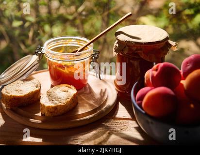 Stillleben einer hausgemachten Aprikosenkonfitüre, Brotscheiben und köstliche reife Früchte auf Holztisch, im Naturhintergrund Stockfoto