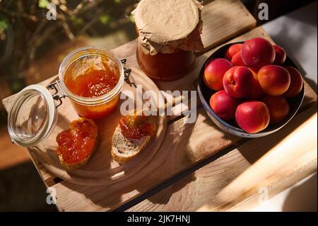 Blick von oben auf eine hausgemachte Aprikosenkonfitüre, Brotscheiben und köstliche reife Früchte auf einem Holztisch im Hintergrund der Natur Stockfoto