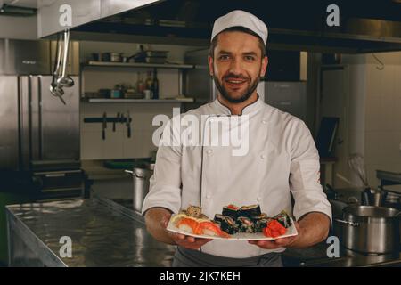 Portrait eines fröhlichen Küchenchefs mit gekochtem traditionellem japanischen Sushi Stockfoto