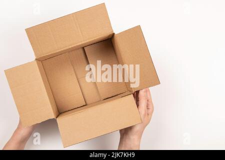 Weibliche Hände mit leerem offenen braunen Pappkarton auf weißem Hintergrund. Draufsicht Stockfoto