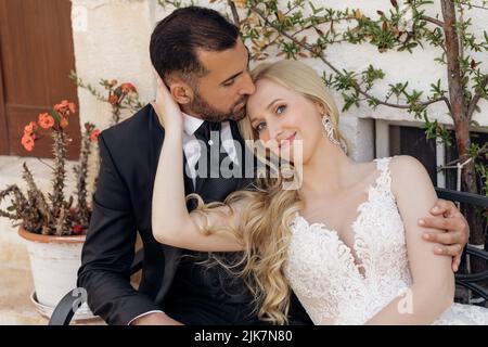 Porträt eines glückseligen Paares, das auf einer alten Straße in der Nähe der roten Blume, dem Baum Commiphora, sitzt. Hochzeit, Hochzeitsreise. Stockfoto