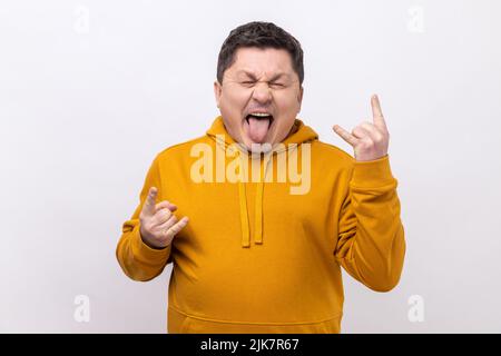 Rock 'n' Roll. Lustiger junger Erwachsener, der mit Rock-Singen steht, schreiend schreiend mit aufgeregt Gesichtsausdruck, trägt einen Hoodie im urbanen Stil. Innenaufnahme des Studios isoliert auf weißem Hintergrund. Stockfoto