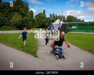 Orford Park, Warrington, Ceshire - 31. Juni 2022. Der Veteran der Streitkräfte, der 51-jährige Ste Hughes, der im Dienst verletzt wurde und sich drei Wirbelsäulenoperationen und vier Gehirnoperationen unterzogen hatte, verbrachte 24 Stunden mit seinem para Nordic Roller Sitski im Orford Park, um erneut Geld für eine Wohltätigkeitsorganisation zu sammeln, wird von Kindern, die mit ihm zusammen liefen, ermutigt. Quelle: John Hopkins/Alamy Live News Stockfoto