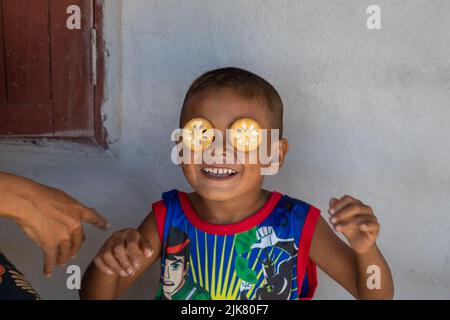 Ein kleiner thailändischer Junge mit Keksen über den Augen und einem Lächeln. Trägt ein Ben 10 T-Shirt Stockfoto