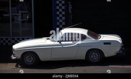 Ein weißes Volvo P1800 S-Auto, das in hellem Sonnenlicht geparkt und von Schatten umgeben ist Stockfoto