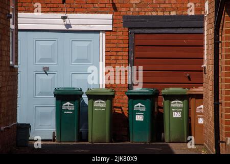 Grüne Mülltonnen vor zwei Garagentüren auf einer gemeinsamen Fahrt in England Stockfoto