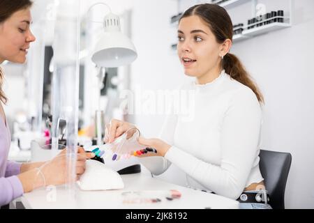 Junge weibliche Manikuristin zeigt Palette von Nagellacken an Frau Klientin Stockfoto