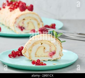 Gebackene Meringue-Rolle mit roten Beeren auf einem runden Teller, weißer Hintergrund Stockfoto