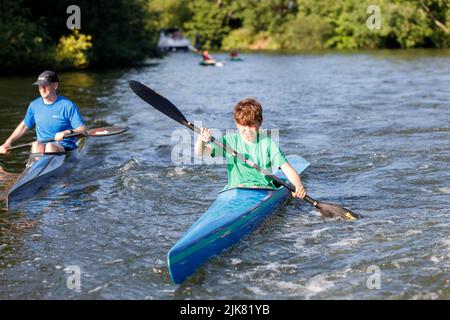 An einem sonnigen Sommertag paddelt ein junger Kajakmännchen an der Themse neben einem älteren Kajakfahrer. K1 Rennkajaks Stockfoto