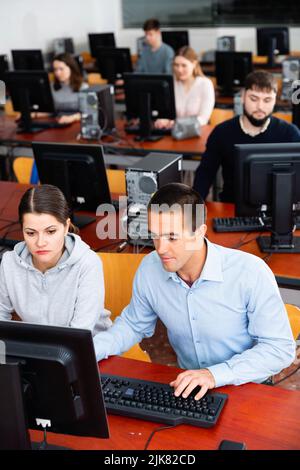 Informatiklehrer überwacht die Ausführung einer Programmieraufgabe in einer Computerklasse Stockfoto