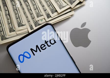 Meta-Firmenlogo auf dem Smartphone gesehen, die auf dem macbook mit verschwommenem Apfel-Logo und US-Dollar gesetzt wird. Konzept. Stafford, Großbritannien, 20. Juli 2022 Stockfoto