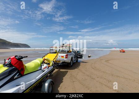 RNLI Rettungsschwimmer am Strand. Ein RNLI Patrouille Pickup Truck sitzt auf einem Strand in Cornwall England mit einem Wellenläufer auf einem Anhänger dahinter Stockfoto