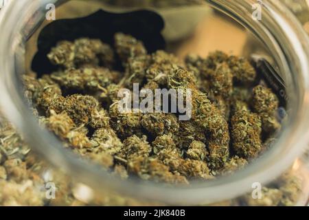 Nahaufnahme von trockenen und getrimmten Cannabisknospen, die in einem transparenten Glasglas aufbewahrt werden. Konzept der alternativen Medizin. Angstlinderung. Hochwertige Fotos Stockfoto