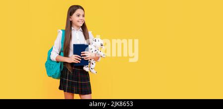 Glückliches Kind mit Rucksack Spielzeug und Buch in Schuluniform voller Länge auf gelbem Hintergrund, Studie. Banner der Schülerin. Schülerin Stockfoto