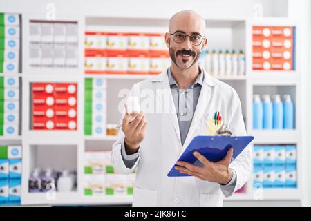 Junger hispanic-Mann Apotheker hält Zwischenablage und Pillen in der Apotheke Stockfoto