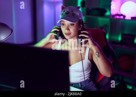 Junge schöne hispanische Frau streamer hält Kopfhörer im Spielzimmer Stockfoto