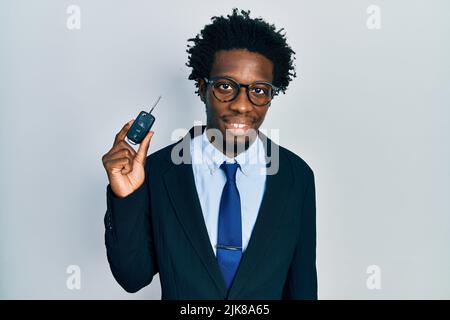 Junger afroamerikanischer Mann, der den Schlüssel eines neuen Autos hält, sieht positiv und glücklich aus und lächelt mit einem selbstbewussten Lächeln, das Zähne zeigt Stockfoto