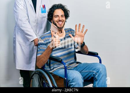 Gutaussehender hispanischer Mann, der auf dem Rollstuhl sitzt und einen Halsband trägt und mit den sechs Fingern nach oben zeigt, während er selbstbewusst und glücklich lächelt. Stockfoto