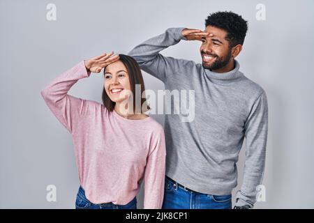 Junge hispanische Paare stehen zusammen sehr glücklich und lächelnd und schauen weit weg mit der Hand über dem Kopf. Suchkonzept. Stockfoto