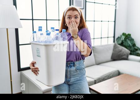 Junge Rotschopf Frau hält Recycling-Papierkorb mit Plastikflaschen lachend und verlegen kichern über den Mund mit Händen, Klatsch und Skandal c Stockfoto