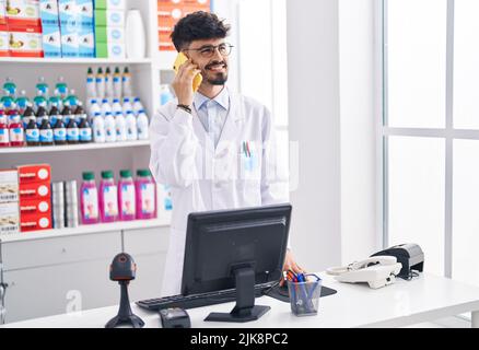 Junger hispanischer Apotheker, der auf dem Smartphone spricht und in der Apotheke arbeitet Stockfoto