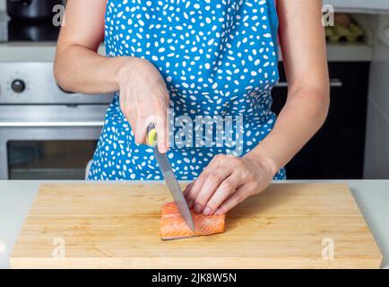 Frau schneidet frisches Lachsfilet auf Holzbrett Stockfoto