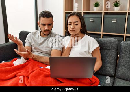 Junge lateinamerikanische kranke Paare, die zu Hause eine medizinische Fernsulation mit einem Laptop haben. Stockfoto