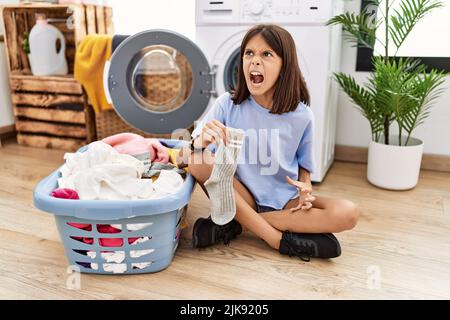 Junge hispanische Mädchen tun Wäsche mit Socken wütend und wütend Schreien frustriert und wütend, schreiend vor Wut. Wut und aggressive Konzept. Stockfoto