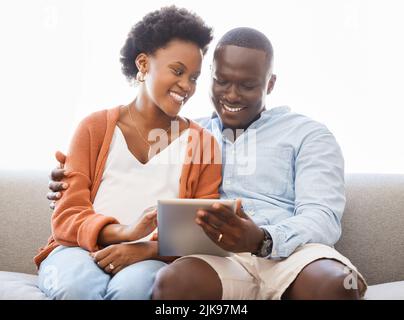 Auf der Suche nach einem neuen Zuhause. Ein junges Paar sitzt auf der Couch, während es zu Hause ein digitales Tablet benutzt. Stockfoto
