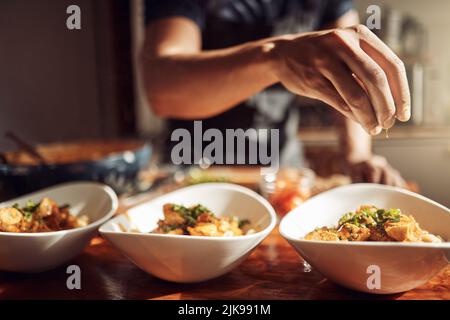 Kulinarische Magie ergießt sich von seinen Fingerspitzen. Ein unverkennbarer Mann bereitet zu Hause ein köstliches Essen zu. Stockfoto