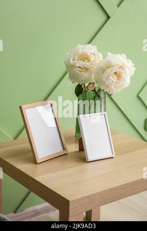 Leere Bilderrahmen und Vase mit Blumenstrauß auf dem Tisch in der Nähe der grünen Wand Stockfoto