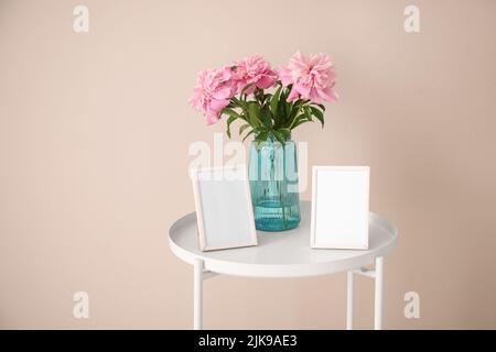 Leere Bilderrahmen und Vase mit Blumenstrauß auf weißem Tisch in der Nähe einer hellen Wand Stockfoto