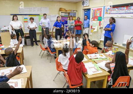 Miami Florida, Frederick Douglass Elementary School Hispanic Studenten jungen Schwarze Mädchen Klassenzimmer heben die Hände, Besucher von Anwaltskanzlei spenden Bücher Stockfoto