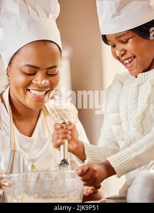 Vergessen Sie nicht, ein wenig Liebe hinzuzufügen. Eine Mutter und ihre Tochter backen in der Küche zu Hause. Stockfoto