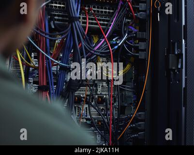 Organisieren wir diese Verkabelung. Ein nicht erkennbarer männlicher IT-Support-Agent, der in einem dunklen Netzwerkserverraum arbeitet. Stockfoto