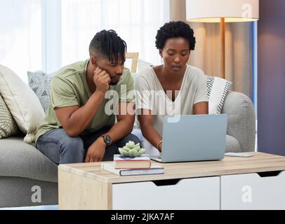 Was sehen wir heute: Ein junges Paar, das einen Laptop benutzt, während es zu Hause auf der Couch sitzt. Stockfoto