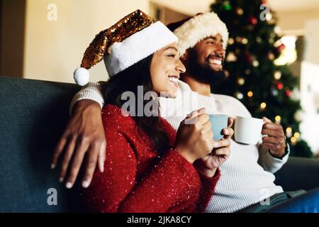 Heiße Schokolade und frohe Weihnachtserinnerungen. Ein glückliches junges Paar, das sich zu Hause auf dem Sofa entspannt und zu Weihnachten warme Getränke trinkt. Stockfoto