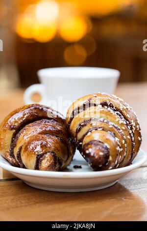 Probieren Sie Schokoladencroissant wie Rugelach und eine Tasse Kaffee auf einem Holztisch in einem Restaurant Stockfoto